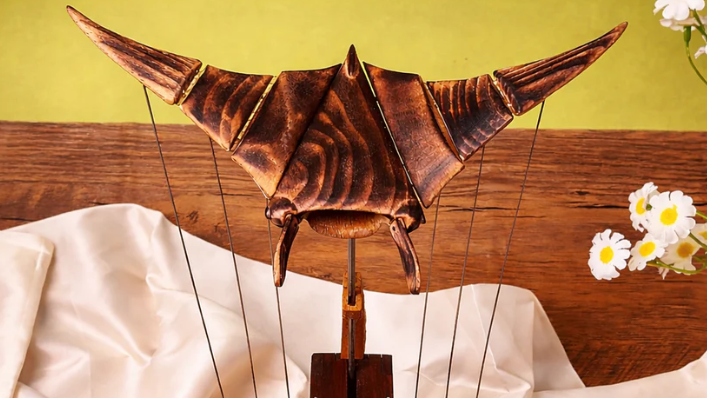 Wooden model of a bat on a wooden base with flowers in the background