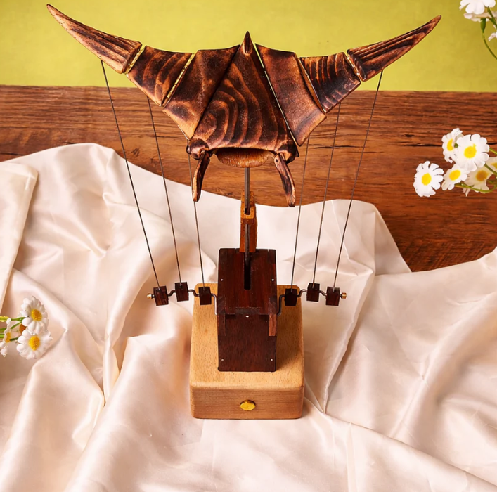 Wooden model of a bat on a wooden base with flowers in the background